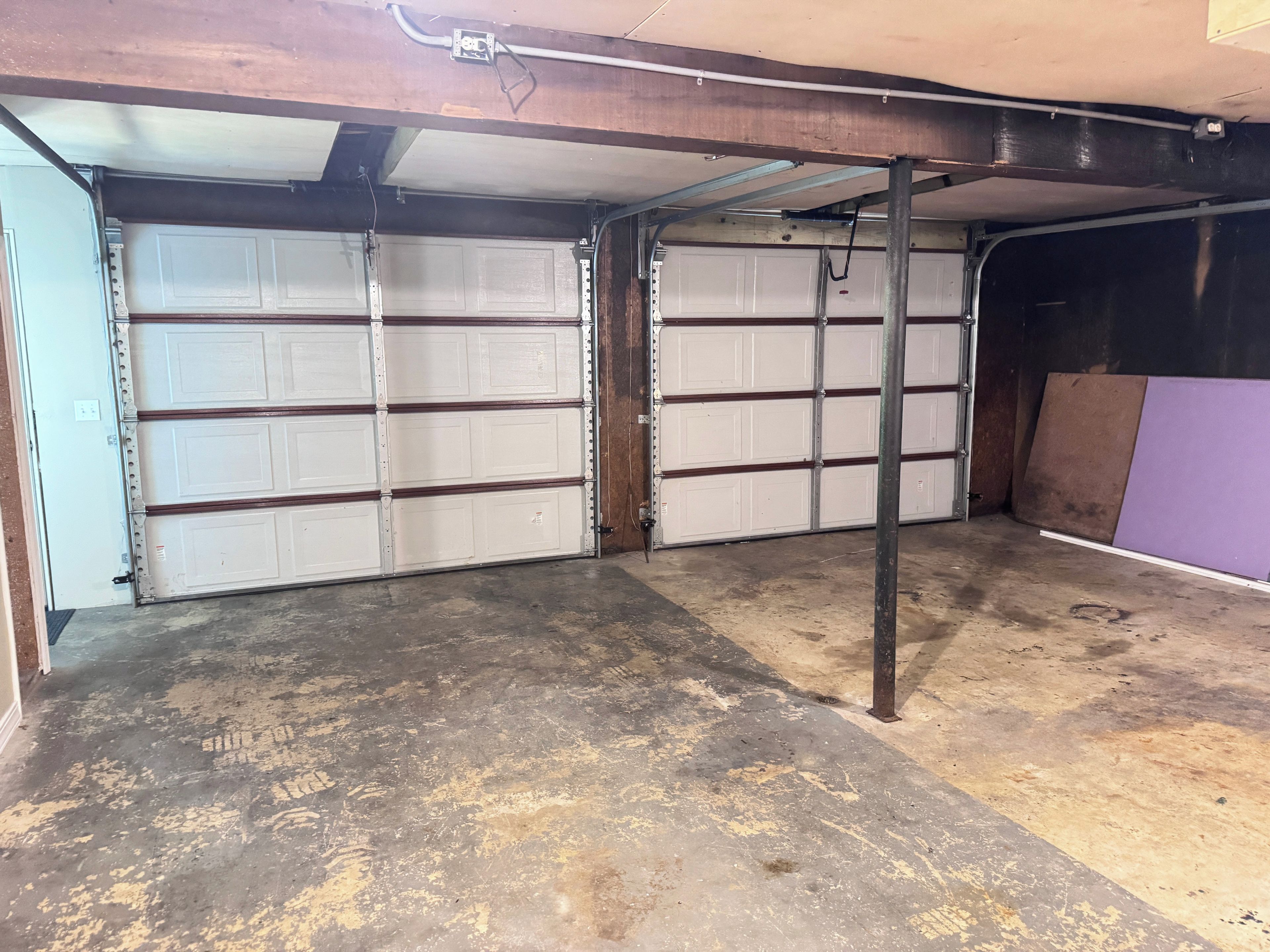 A garage with two white garage doors, a concrete floor, and a metal beam structure.