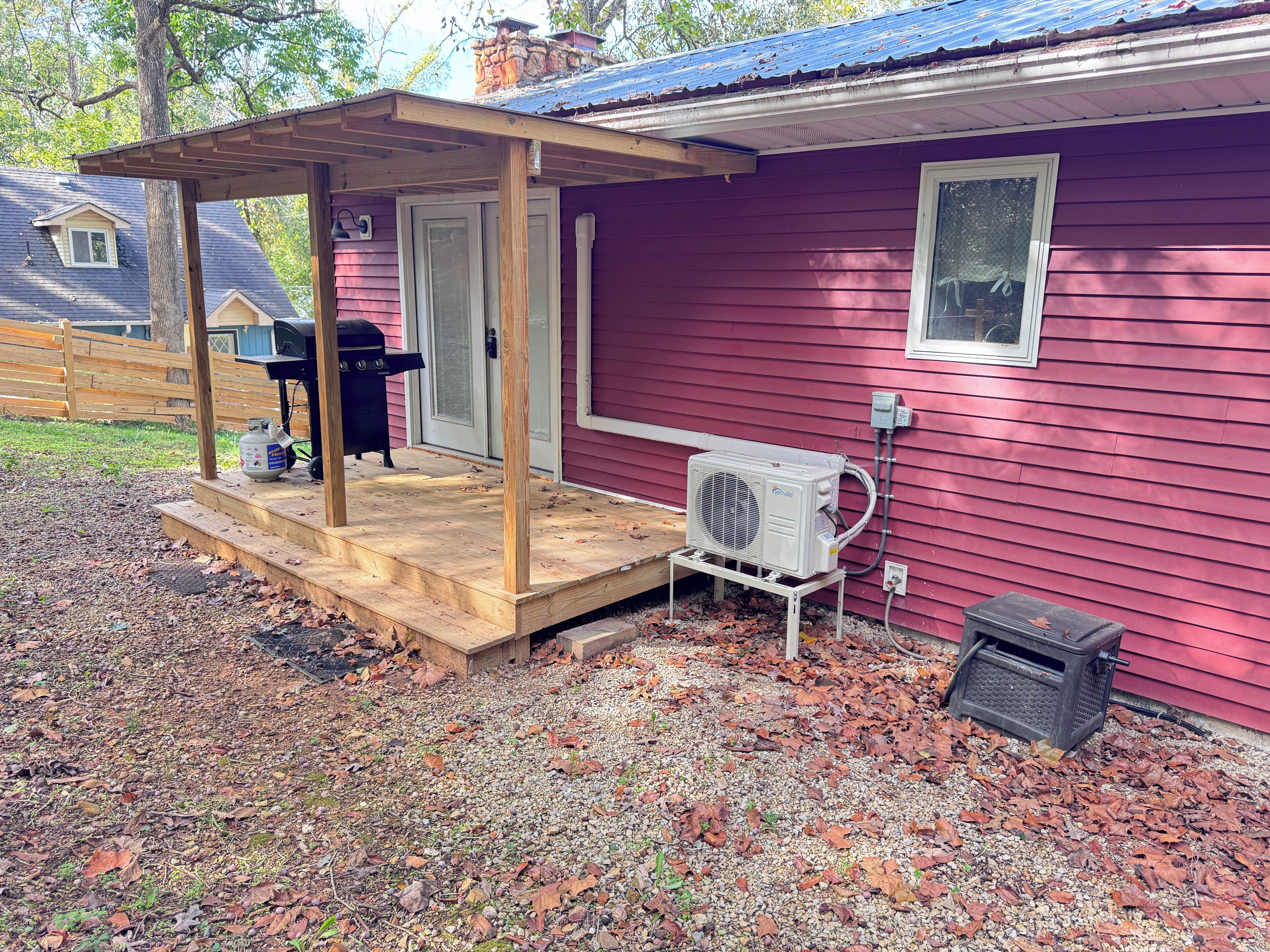 Ein rotes Haus mit überdachter Veranda, Grill und Klimaanlage.