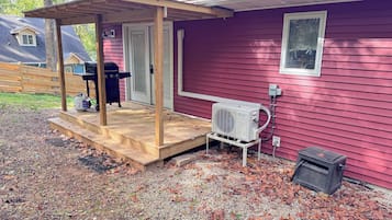 A red house with a covered porch, a grill, and an air conditioning unit.