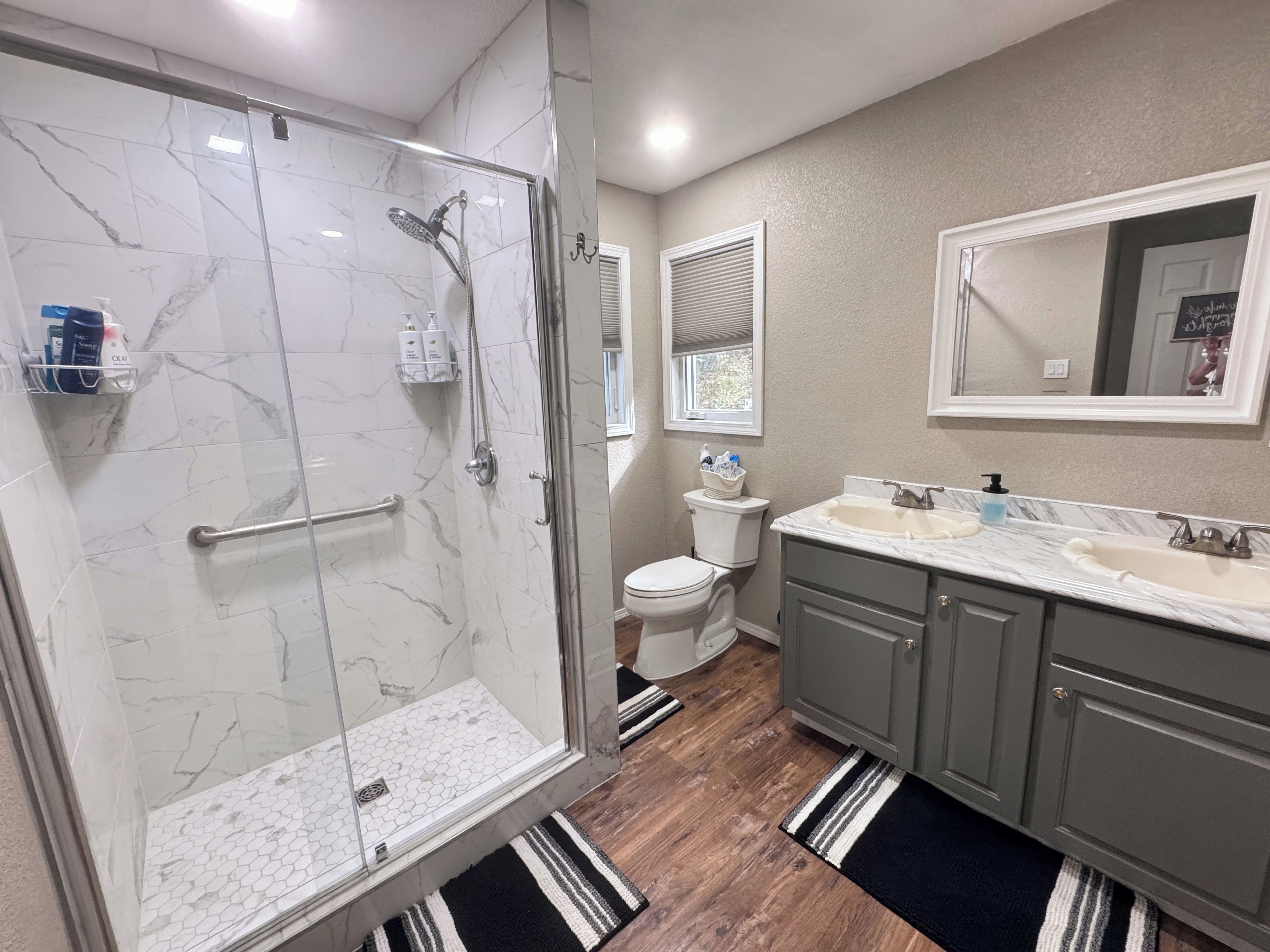 A bathroom with a glass-enclosed shower, a toilet, a sink with a marble countertop, and a mirror above the sink.