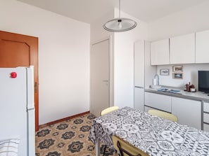 A compact kitchen with a refrigerator, a dining table with a patterned tablecloth, and a hanging light fixture. - Casa Lara (Carloforte)