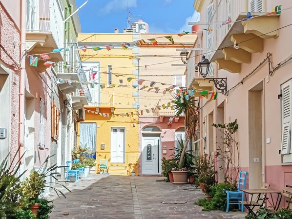 Una calle estrecha flanqueada por edificios, algunos con balcones y plantas en macetas.