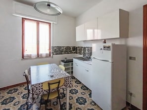 A compact kitchen with a dining table, chairs, a refrigerator, and a window with curtains. - Casa Lara (Carloforte)