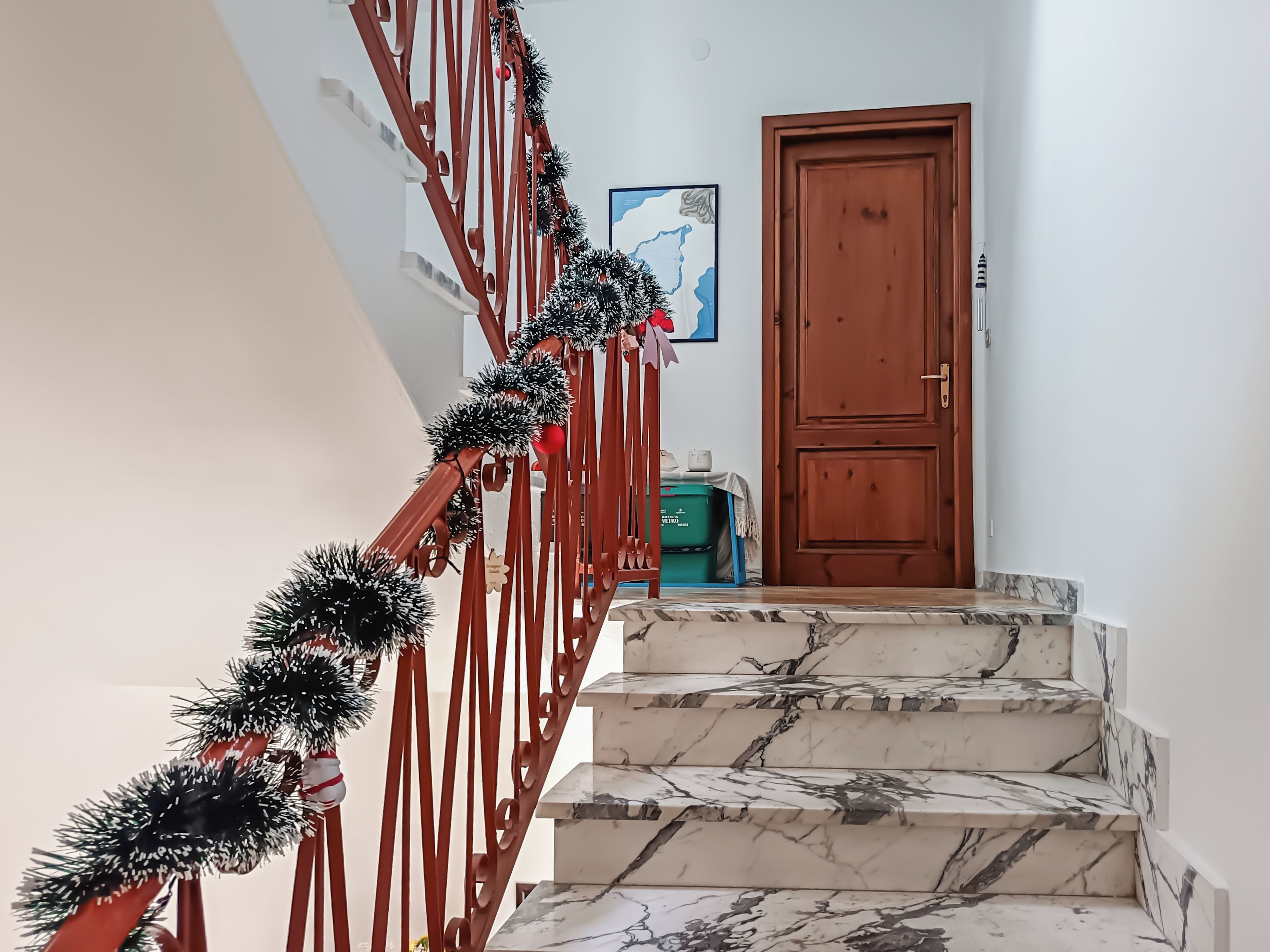 Uma escadaria com corrimão vermelho e enfeites de tinsel preto, levando a uma porta de madeira.
