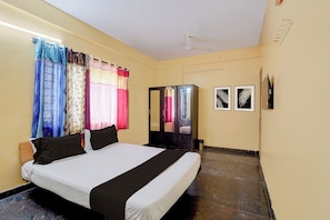 Una habitación de hotel con cama, cortinas, un armario y dos cuadros en la pared.