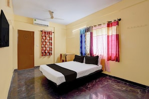 Una habitación de hotel con cama, ventilador de techo, aire acondicionado, una puerta y cortinas.