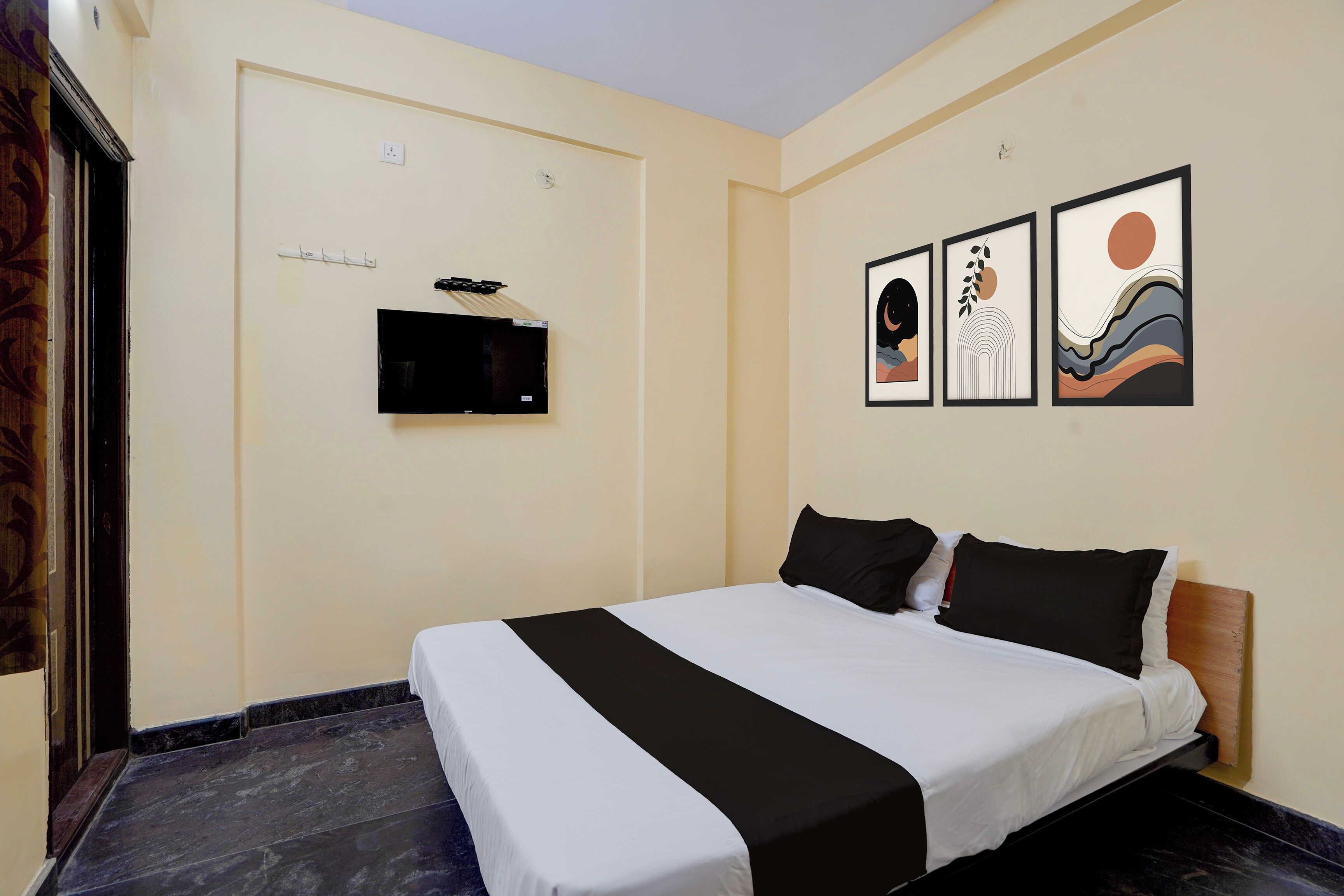 Ein Hotelzimmer mit einem Bett, einem flachbildfernseher an der Wand und drei gerahmten Kunstwerken über dem Bett.
