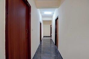 Un pasillo con puertas de madera y suelo de baldosas, que conduce a una habitación con techo blanco y una lámpara.