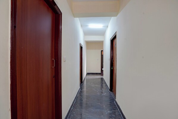A corridor with wooden doors and a tiled floor, leading to a room with a white ceiling and a light fixture. - Hotel O Royal Treat (Bangalore)