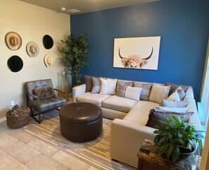 A living room with a blue accent wall, a sofa, a chair, a round ottoman, and a bull's head artwork. - 3-bedroom townhome in Plano’s entertainment and corporate area. Comfy Texas vibe (Plano)