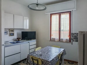 A compact kitchen with a dining table, a television, and a window with curtains. - Casa Lara - Charming Apartment in the Heart of Carloforte's Historic Center (Carloforte)