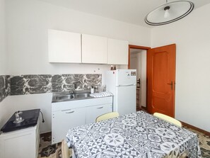 A compact kitchen with white cabinets, a marble backsplash, a white refrigerator, and a patterned tablecloth-covered dining table. - Casa Lara - Charming Apartment in the Heart of Carloforte's Historic Center (Carloforte)