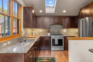 A modern kitchen with dark wood cabinets, granite countertops, stainless steel appliances, and a skylight.