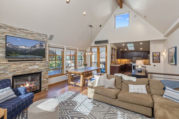 A spacious living room with a fireplace, a large TV mounted on a stone wall, and a cozy seating area with a patterned rug.
