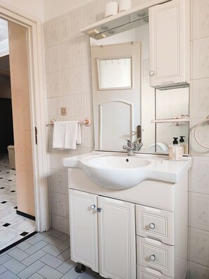 Un bagno con un lavandino bianco, uno specchio e mobiletti.