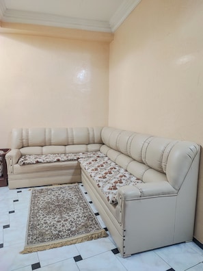 A beige sectional sofa with a floral throw blanket and a patterned rug in a room with cream walls and a tiled floor. - Traditional, family-friendly apartment in the heart of Tangier (Tanger)