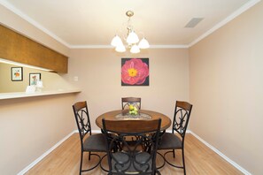 A dining area with a round table, four chairs, a chandelier, and a wall-mounted flower painting. - Urban Oasis: In the Medical Center (San Antonio)