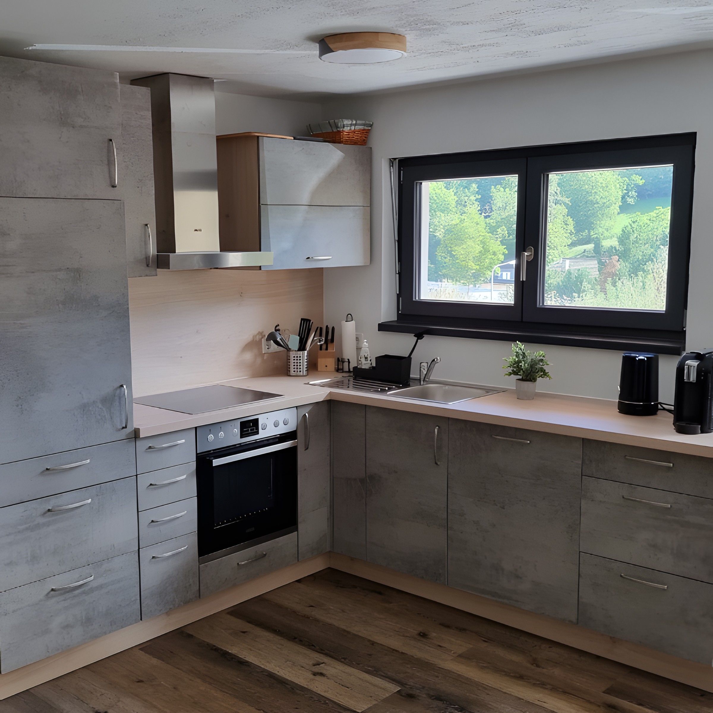 Eine moderne Küche mit grauen Schränken, einem eingebauten Backofen, einer Spüle und einem Fenster mit Blick ins Grüne.