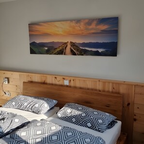 Un dormitorio con cabecera de madera, cama con ropa de cama estampada y un cuadro de un paisaje de atardecer en la pared.