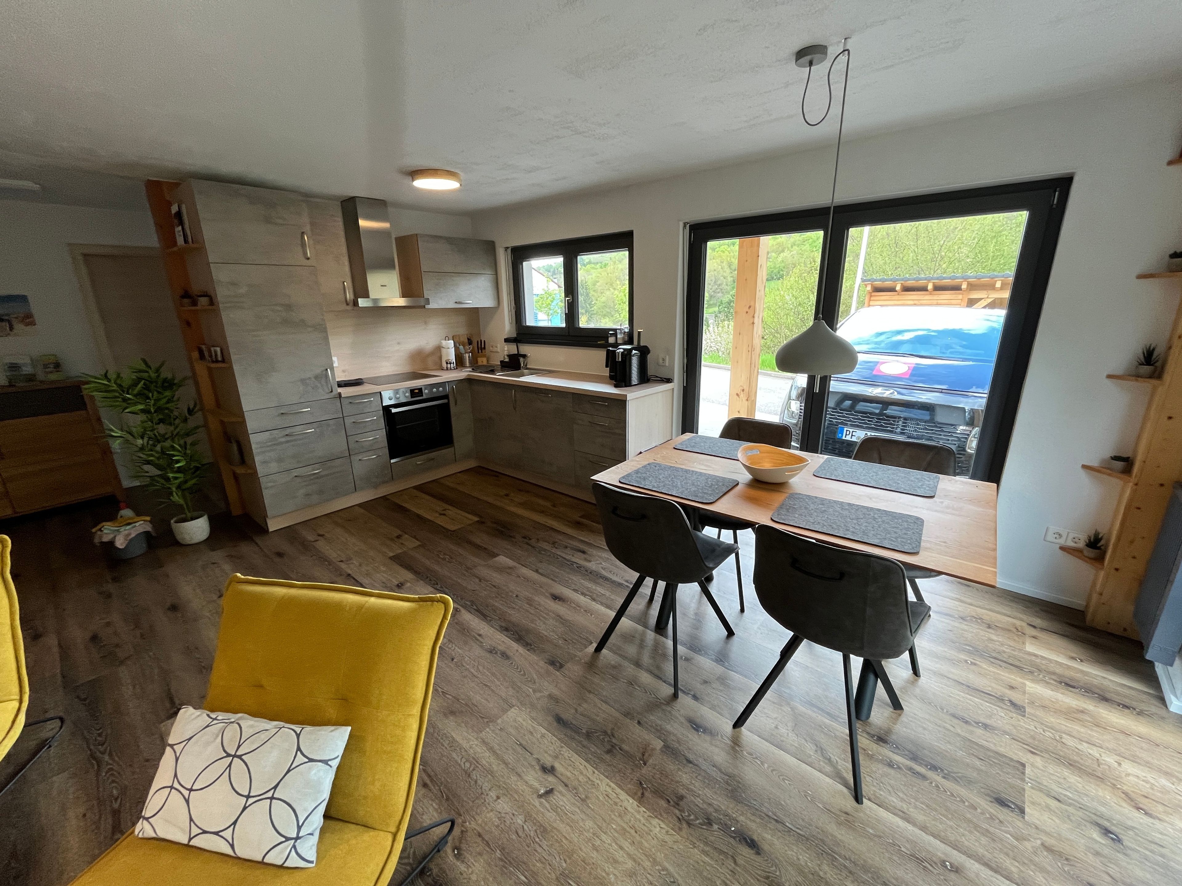 A modern kitchen with a dining area, wooden flooring, and a view of the outdoors.