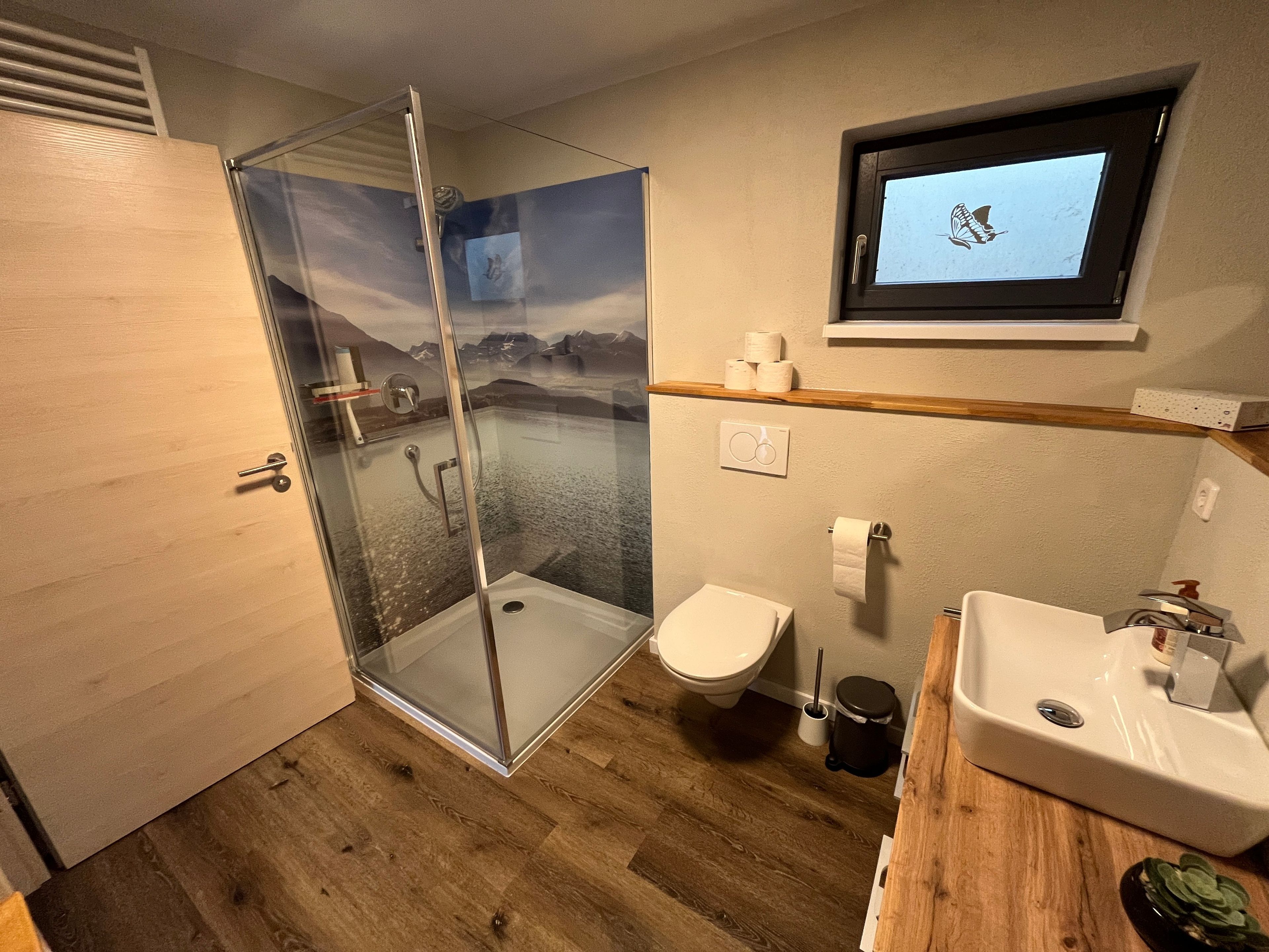 Ein Badezimmer mit einer Duschkabine, Toilette, Waschbecken und einem an der Wand montierten Fernseher, der einen Schmetterling zeigt.