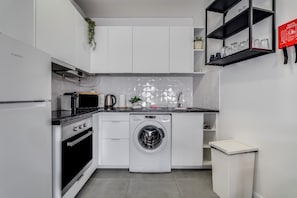 Een moderne keuken met witte kasten, een wasmachine, een magnetron en een spoelbak.