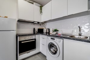 A compact kitchen with a built-in oven, microwave, and washing machine, a stainless steel sink, and white cabinetry. - Casa Sol e Sal  3-Min Walk to Beach & Old Town (Albufeira)