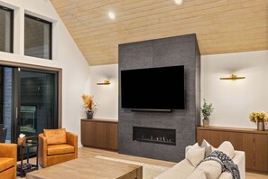 A modern living room with a flat-screen TV mounted on a dark wall, wooden flooring, and a fireplace. - Lux 6 BdRm, Media Rm, Built-in BBQ, Chefs Kitch (Cle Elum)