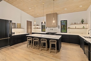 Una cocina moderna con una isla grande, taburetes de bar, iluminación colgante y vistas al exterior.