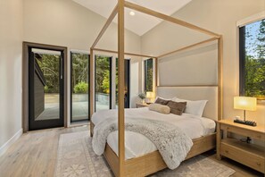 A four-poster bed with a wooden frame, a nightstand with a lamp, and a view of a garden through the glass doors. - Lux 6 BdRm, Media Rm, Built-in BBQ, Chefs Kitch (Cle Elum)
