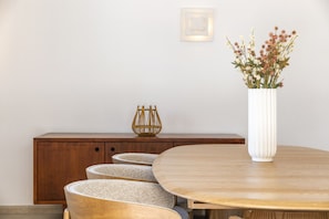 A dining area with a round wooden table, a white vase with flowers, and a wooden cabinet with a woven basket. - New! Quinta Lamy - Villa with Pool near Carvoeiro (Lagoa)