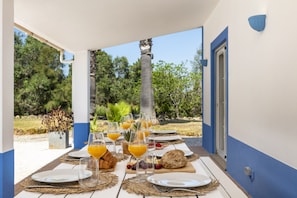 An outdoor dining area with a table set for breakfast, including plates, glasses, and a loaf of bread. - New! Quinta Lamy - Villa with Pool near Carvoeiro (Lagoa)