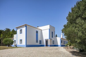 A two-story building with a white and blue facade, a cobblestone driveway, and a clear blue sky. - New! Quinta Lamy - Villa with Pool near Carvoeiro (Lagoa)