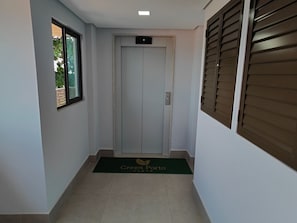 A hallway with a door, a window, and a door mat with a logo. - Green P. Ap. 307 Leo Milán (Ipojuca)