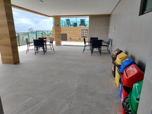 A spacious indoor area with a balcony overlooking a body of water, furnished with tables and chairs. - Green P. Ap. 307 Leo Milán (Ipojuca)