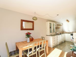 A dining area with a wooden table and chairs, a vase with flowers, a kitchen with white cabinets, and a mirror on the wall. - Moness Garden Studio (Aberfeldy)
