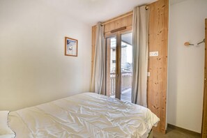 Ein Schlafzimmer mit einem Bett, einem Fenster mit Vorhängen, einer Holztür und einem kleinen Bild an der Wand.