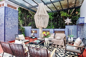 A cozy patio area with wicker furniture, a hanging macrame light fixture, and a patterned tiled wall. - Timeless Charm in Condesa 6BR, Perfect Terrace (Mexico City)