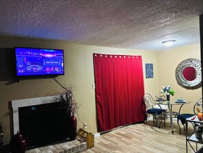 Un salon comprenant un téléviseur, une cheminée, une table à manger avec des chaises, un rideau rouge et un miroir décoratif.