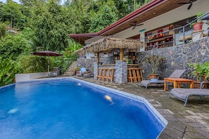 A swimming pool with a bar area, lounge chairs, and a stone wall.
