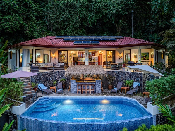 A resort with a swimming pool, outdoor seating, and a thatched-roof bar area.