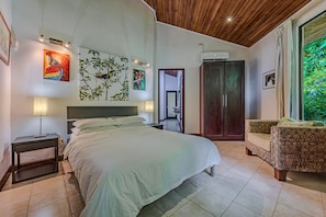 Une chambre à coucher avec un lit, des tables de chevet, une armoire et une vue sur la verdure.