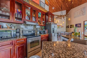 A kitchen with granite countertops, stainless steel appliances, wooden cabinets, and a hanging light fixture. - Villa Pacifica- Spectacular View, Gated Community (Savegre)