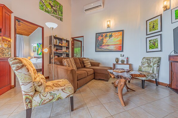 A living room with a sectional sofa, a patterned armchair, a coffee table with a wooden centerpiece, and a bookshelf.