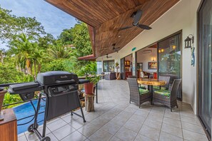 An outdoor patio with a barbecue grill, wicker furniture, and a view of lush greenery. - Villa Pacifica- Spectacular View, Gated Community (Savegre)
