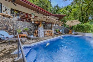 A pool area with lounge chairs, a bar, and a stone wall.