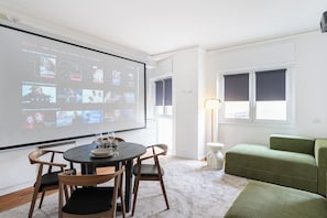 Una sala moderna con una pantalla grande mostrando una selección de películas, una mesa de comedor con sillas y un sofá verde.