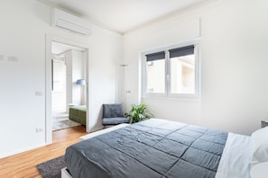 Un dormitorio con cama, una silla, una planta en maceta y un ventanal.