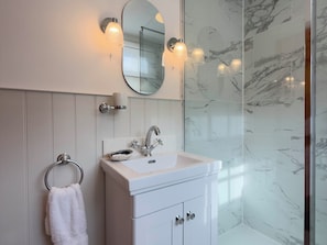 A bathroom with a white vanity, a round mirror, and a glass shower enclosure. - Redwood Cottage (Bristol)