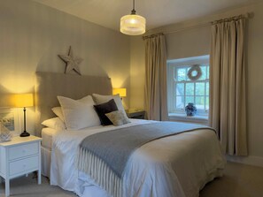 A bedroom with a bed, bedside lamps, a star decoration, a window with curtains, and a hanging wreath. - Redwood Cottage (Bristol)